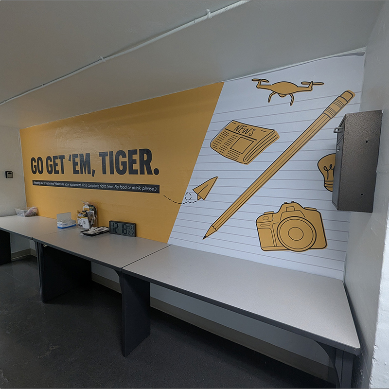 Wall vinyl "Go Get 'Em, Tiger" with pencil, drone, newspaper and camera icons.
